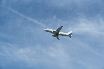 Fototapeta premium White passenger airplane climbing in the blue sky with light cirrus clouds after takeoff. White aircraft taking off and gaining altitude against a beautiful blue sky and wispy clouds.