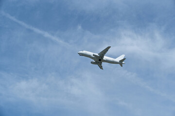 Fototapeta premium White passenger airplane climbing in the blue sky with light cirrus clouds after takeoff. White aircraft taking off and gaining altitude against a beautiful blue sky and wispy clouds.