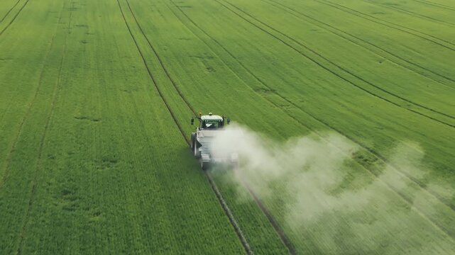 Drone aerial - tractor spreading nitrogen fertilizer on farmland with dust cloud