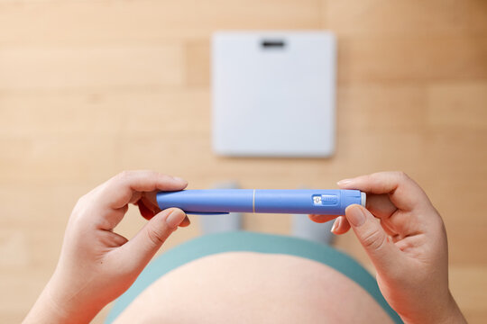 A horizontal close up of a young woman holding pre-filled pen injector with semaglutide 
A young woman holding pre-filled pen injector with semaglutide on floor and scales background