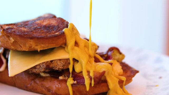 to pour mustard on layers of a Reuben sandwich filled with corned beef, Swiss cheese, and sauerkraut, placed on a wooden board, highlighting a tasty meal perfect for lunchtime.