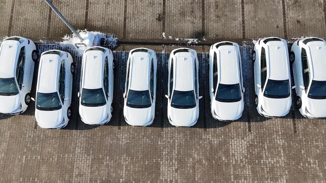 Aerial view of multiple new white cars parked in a straight line on a snow-covered parking lot at a car dealership, commercial auto showroom display, brand new vehicles for sale, modern automotive ret