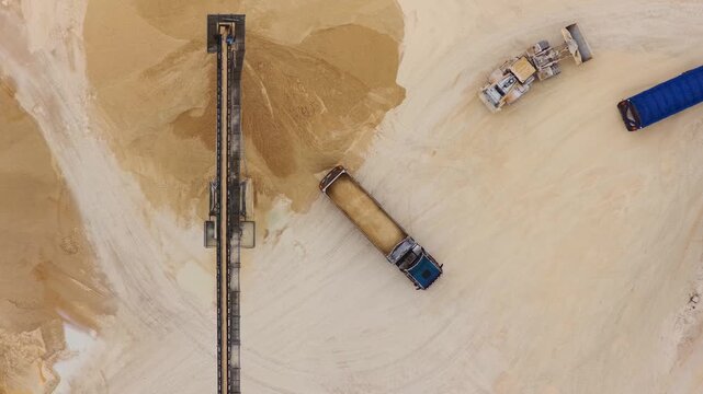 Aerial view of two trucks near a sand pile, their shadows stark against the light sand, creating a compelling contrast, Arsoli, Lazio, Italy.