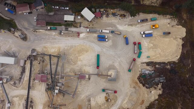 Aerial view of trucks loading materials in a vast quarry, contrasting the industrial activity with the surrounding natural landscape, Arsoli, Lazio, Italy.