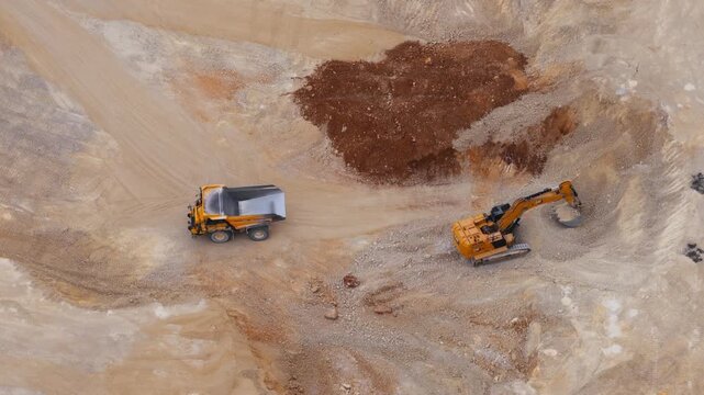 Aerial view of yellow machinery, a truck and excavator, contrasted against the light beige and brown earth of a quarry, Arsoli, Lazio, Italy.