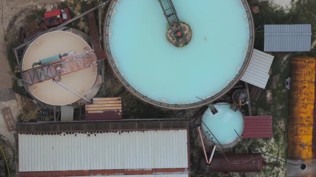 Aerial view of tanks with blue and beige liquids, surrounded by industrial buildings and rusty containers, Arsoli, Lazio, Italy.