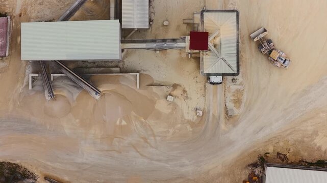 Aerial view of industrial buildings and machinery set against a backdrop of light brown earth, Arsoli, Lazio, Italy.