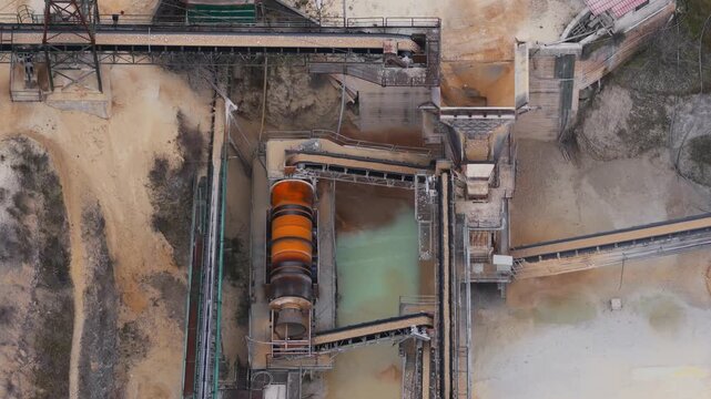 Aerial view of an industrial site featuring pools with contrasting colors and textures, surrounded by sandy terrain, Arsoli, Lazio, Italy.