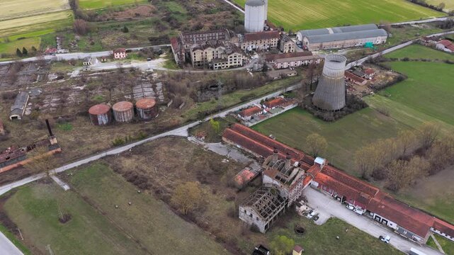 Aerial view of weathered industrial buildings and cooling tower stand out against fields and roads, creating a striking juxtaposition of decay and nature, Avezzano, Abruzzo, Italy.