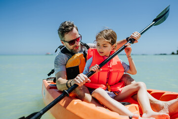 Obraz premium Father kayaking with daughter on calm sea during family summer vacation.