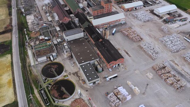 Aerial view of an industrial plant with circular tanks and stacked materials in a yard, presenting a mix of textures and tones, Avezzano, Abruzzo, Italy.