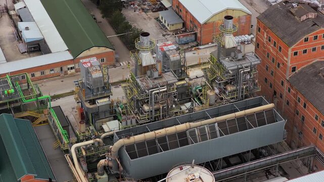 Aerial view of a sprawling industrial complex featuring a central processing unit with an array of pipes, tanks, and chimneys, Avezzano, Abruzzo, Italy.