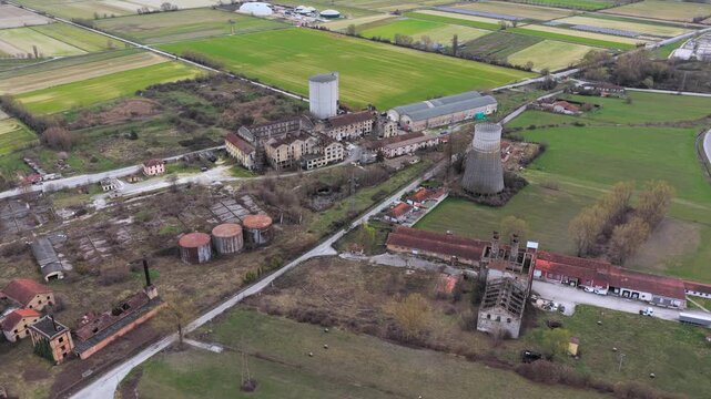 Aerial view of the industrial site revealing a mix of decaying buildings, tanks, and structures, contrasting with the surrounding patchwork of green and brown fields, Avezzano, Abruzzo, Italy.