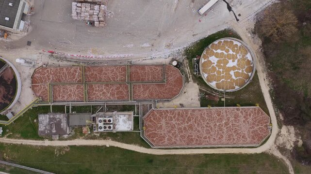 Aerial view of a water treatment plant featuring tanks and settling ponds with earthy tones against the muted landscape, Avezzano, Abruzzo, Italy.