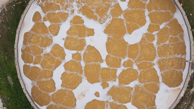 Aerial view of a circular processing tank with contrasting brown and white liquid swirling, creating an abstract pattern, Avezzano, Abruzzo, Italy.