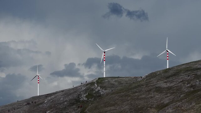 Aerial view of several wind turbines standing tall on a grassy hill under a cloudy sky creating a stark contrast, Cocullo, Abruzzo, Italy.