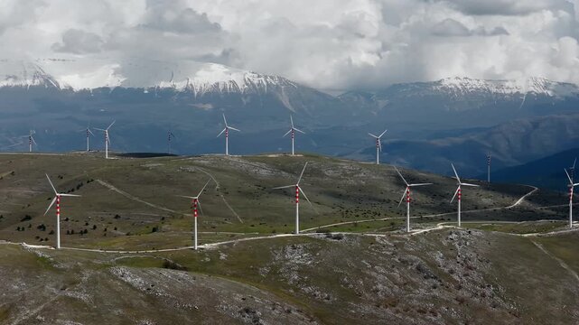 Aerial view of many wind turbines dotting the rolling hills, with snow-capped mountains in the background, Cocullo, Abruzzo, Italy.