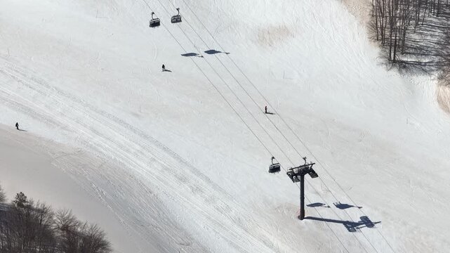 Aerial view of skiers and a ski lift on the snowy slopes of Mount Etna, a contrast of bright white snow and dark ski lift structures, Piano Provenzana, Sicilia, Italy.