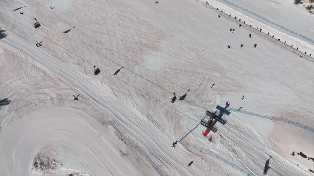 Aerial view of ski lift and skiers on the snowy slopes of Mount Etna, a contrast of white snow and dark figures, Piano Provenzana, Sicilia, Italy.