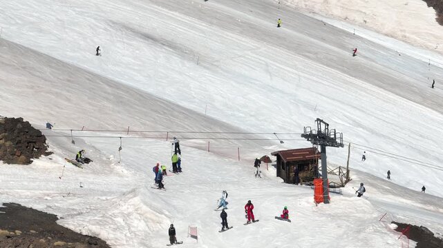 Aerial view of skiers descending the snowy slopes of Mount Etna, a stark contrast between the white snow and dark volcanic rock, Piano Provenzana, Sicilia, Italy.