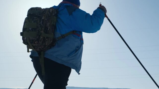 Camera follows from side overweight man struggling to walk on skis using poles. Tourist with backpack makes effort to move on skis. Difficult distance due to excess weight