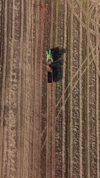 Tractor in Field at Harvest Time: An agricultural tractor with a trailer is seen from above, working in a vast field during the harvest season.