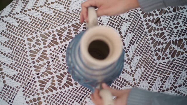 Vintage lace tablecloth ceramic jug overhead, sequence captures crocheted pattern and blue pottery teapot, hands placing handle into frame, soft natural light and gentle shadows, intimate cottagecore