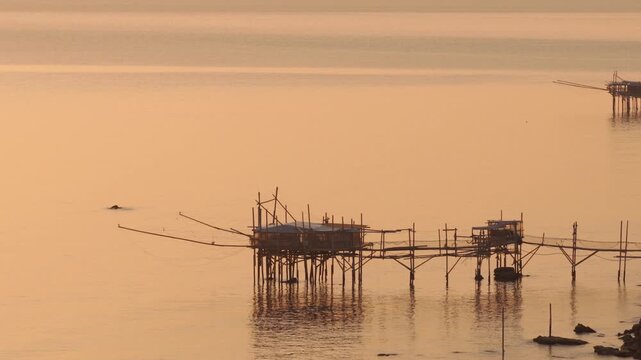 Aerial view of traditional trabucchi fishing platforms standing on stilts in the sea, reflecting the golden light of dusk, San Vito Chietino, Abruzzo, Italy.