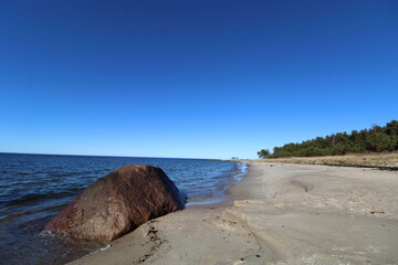 Large boulder on empty sandy shoreline under clear blue sky © Mattias
