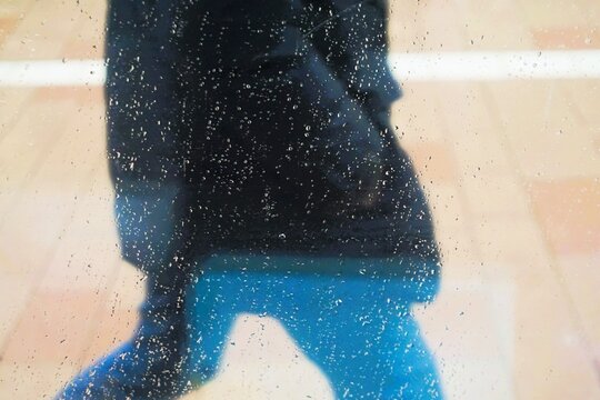 Abstraktes Motiv mit gehendem Mann auf Stra&szlig;e mit schwarzer Jacke und blauer Jeanshose in Stadt bei K&auml;lte, Sturm und Schneeregen am Nachmittag im Winter