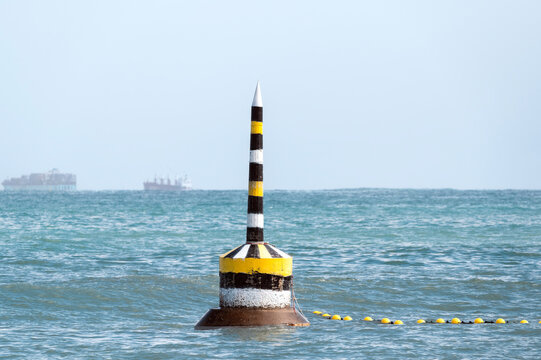 Historic black, white and yellow pylon located at Cottesloe Beach with container ships on the horizon, Perth, Western Australia.