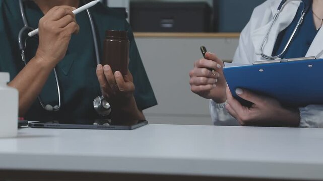 Medical team having a meeting with doctors in white lab coats and surgical scrubs seated at a table discussing a patients working online using computers