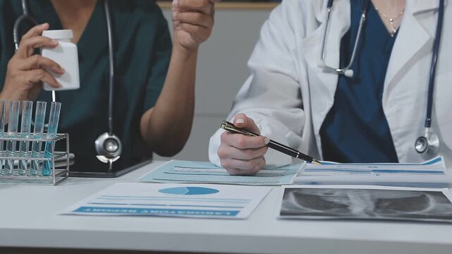 Medical team having a meeting with doctors in white lab coats and surgical scrubs seated at a table discussing a patients working online using computers