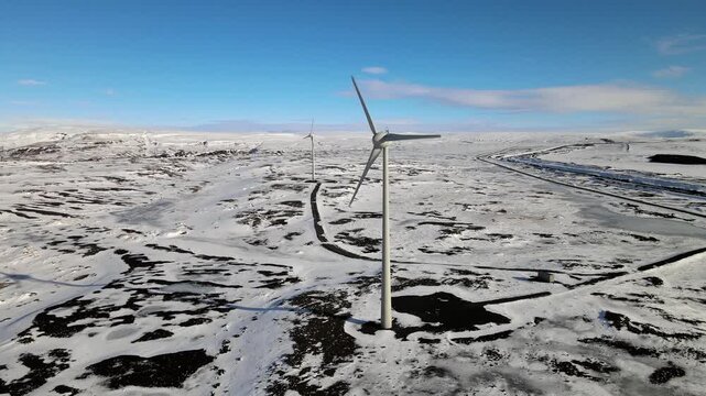 Aerial view of stark white wind turbines contrasting against the dark, snow-dusted terrain creating a striking visual, Skeida- og Gnupverjahreppur, Iceland.