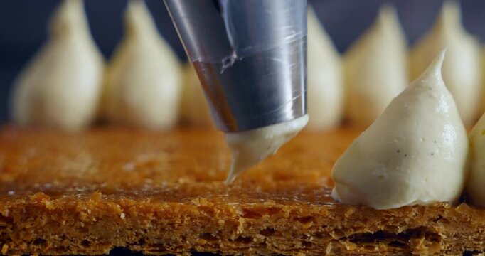 Close-up cinematic shot of a pastry chef decorating a cake with cream using a piping bag. Soft lighting enhances texture and precision.