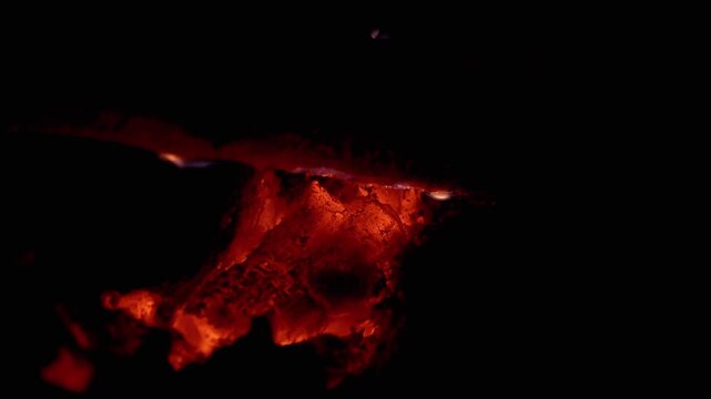 Smoldering embers glow intensely under a piece of wood, creating a warm and inviting atmosphere. Great for projects related to cooking, grilling, and outdoor activities.