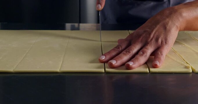 Close-up cinematic shot of a pastry chef cutting raw dough into shapes with knife. Texture and precision emphasized with soft lighting
