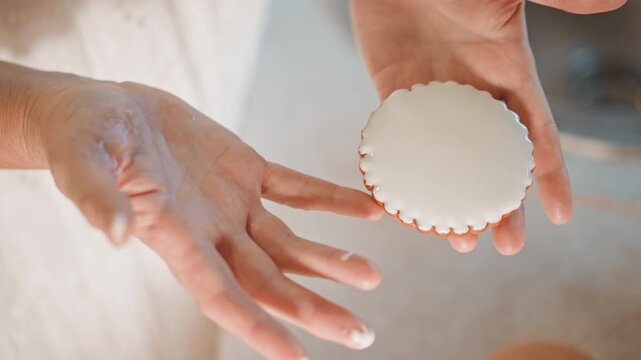 Hands with cookie. Close image of hands grasping frosty pumpkin treat in cozy kitchen. Detailed shot capturing hands softly handling chilled pumpkin cookie amidst flour and gentle light