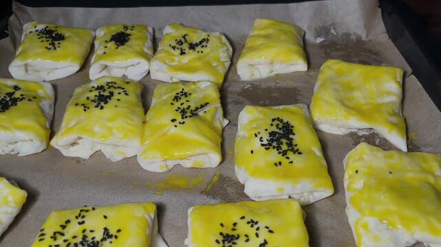A woman&rsquo;s hand sprinkling nigella seeds on the pastries on the baking sheet; the preparation of homemade pastries from traditional Turkish cuisine and their delicious details.