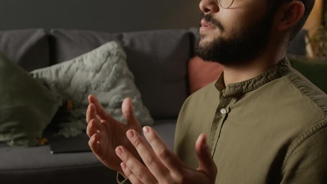 Cinematic close up shot of modern Muslim man turning head during salah finishing daily prayer at home, and following traditional religious rituals, copy space