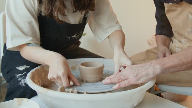 Close up shot of eldely and young craftswomen using string while working on potters wheel together in workshop