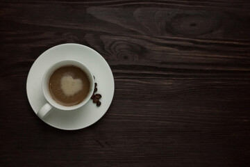 Obraz premium Top view of cappuccino with heart latte art and roasted coffee beans on dark textured background