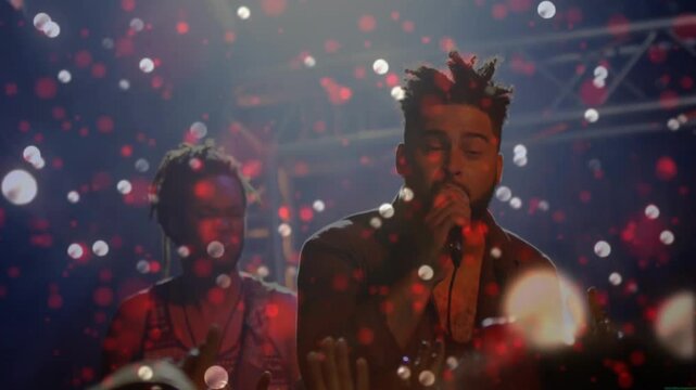 Lead singer starting song, singing into handheld mic, engaging crowd while red white bokeh drifting