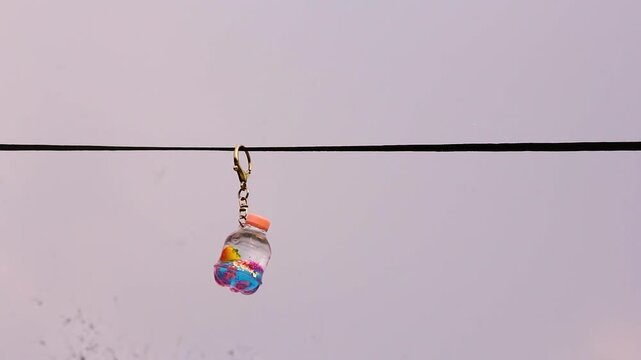 Small decorative bottle keychain hanging on a wire against a pale sky at a medium shot