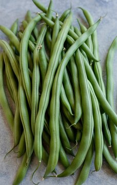 A bunch of long, thin, green haricot vert beans on a grey background