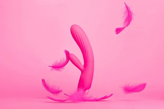 Pink sex toy rabbit shaped female vibrator for women isolated on pink background with feathers flying in the air, gentle feelings, viva magenta monochrome colours