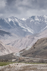 Fototapeta premium The Pamir Highway, a paved road in a valley of rocky mountains, with high mountain ranges and peaks covered with snow and glaciers in the background, a landscape in the Tien Shan Mountains
