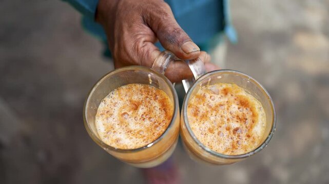 A man holds two steaming cups of milk tea, capturing the warmth of everyday street life in India and Bangladesh, where chai is a beloved tradition, comfort, and daily ritual