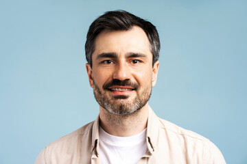 Fototapeta premium Portrait of handsome bearded man wearing casual shirt looking at camera isolated on blue background