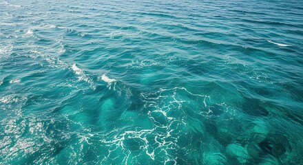 Naklejka premium Crystal clear turquoise ocean water with gentle waves and white foam creating natural patterns. Bright blue-green sea shows shallow areas with visible underwater details. Perfect for travel content.